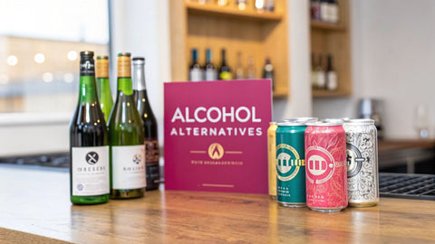 a wooden table with bottles of wine and selters next to a pink sign reading 'alcohol alternatives'