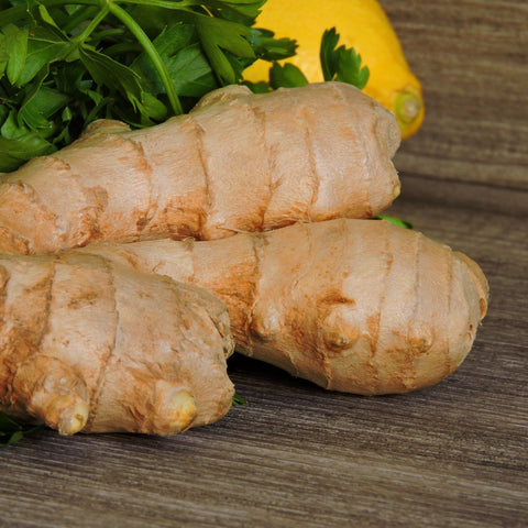 Three pieces of ginger root on a wooden surface with green leaves in the background.